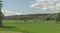 Green fields in beautiful summer sunshine. Small farm and forest in the distance