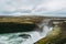 Green fields, black rocks, and turquoise water of Gullfoss waterfall in Iceland.