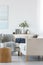 Green flowers in grey vase next to books on wooden console table in bright living room interior