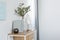 Green flowers in grey vase next to books on wooden console table in bright living room interior