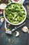 Green fresh organic lettuce leaves in old enameled colander on dark rustic kitchen table with tools and ingredients for salad