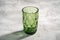 Green glass geometric cup with colorful shadow light rays on stone concrete background