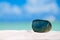 Green glass stone on white sand beach,