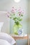 Green glass vase with bouquet of beautiful puppy flowers on table in bedroom.