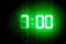 Green glowing digital clocks in the dark show 7:00 time