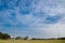 Green grass field with blue cloudy sky and tall spotlight for night sport event.