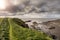 Green grass fields by the ocean and small foot path and rough stone coastline, low cloudy sky. West coast of Ireland. Irish