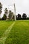 Green grass in foreground in focus, White metal soccer or football goal post with net out of focus