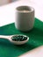 Green hawaiian spirulina in tablespoons pills in wooden spoon on green background with candle at home.