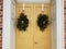 Green holiday wreaths on yellow door of building