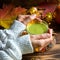 Green Japanese matcha tea with foam in transparent Cup on wooden table in autumn still life. Women`s hand with long white sweater