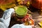 Green Japanese matcha tea with foam in transparent Cup on wooden table in autumn still life. Women`s hand with long white sweater