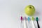 A green juicy strong apple and several colored toothbrushes next to it, on a white background