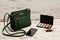 Green ladies handbag, phone, eyeshadow palette and a lipstick on a wooden background