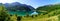Green landscape with lake and high mountains that are reflected in the water, blue sky and sun flare. Panoramic view. Pyrenees,