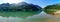 Green landscape with lake and high mountains that are reflected in the water, blue sky and sun flare. Panoramic view. Pyrenees,