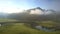 Green landscape with meandering river near hills in fog