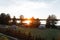 Green lawn with a tent with a gazebo with a trampoline with a wooden fence against the backdrop of an orange sunset and a lake.