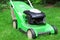 A green lawnmower in the garden. A lawn mower on the green grass. Gardening