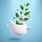 Green leaves fly out of white kettle, herbal tea levitation