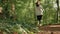 Green leaves on the foreground. Real time. Defocused woman in sports clothes is jogging at forest. Back view. Low angle