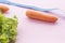 Green lettuce leaves, carrots and a measuring tape on a pink background.