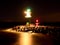 Green lighthouse shinning at the end of stony pier in dark night
