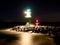 Green lighthouse shinning at the end of stony pier in dark night