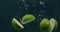 Green limes are thrown into a container of water. Video of fruit in slow motion.