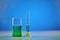 Green liquid in beaker and measuring cylinder, blue background. Laboratory research of Coronavirus. Worldwide pandemic