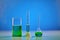 Green liquid in beaker, medical flask and measuring cylinder, blue background. Coronavirus laboratory research