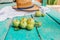 Green little homemade apples in water drops on the green wooden floor, farmer`s shirt and straw hat blurred against the background