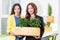 Green living. Two attractive young businesswomen holding a box with plants istanding in modern office. Environmental