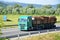 Green MAN truck fully laden by wood drives on slovak D1 highway surrounded by rural landscape.