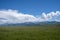 Green meadow with cloudy sky and mountains background. Beautiful meadow scenery. Adventure day. Mountain hiking.