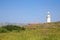 Green meadow, lighthouse, roof of the house and mountains in the