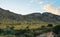 Green meadows with rocks, some trees, steep rocky cliffs background, river flowing in foreground, typical Madagascar landscape in