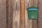 Green metal mail box hanging on right side of wooden house wall