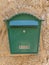 Green metal mail box hanging on yellow concrete house wall