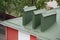 Green metal roof with big chimney pipes and ventilation system. White rain gutter.