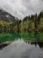 Green mirroring lake in forest and mountains covered by snow