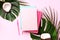 Green monstera, palm leaves, coconut, notebooks over pink background. Female blog writer workspace concept. Flat lay. Top view