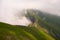 Green mountain with low clouds, mountain hiking trail on the edge