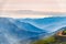 Green mountain slope in dense fog. Layers of mountains in the haze during sunset. Several horses are moving along a mountain road