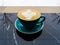 A green mug of cappuccino sits on a black marble table. Cappuccino in the early cold morning. Reflection in the table of trees and