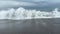 Green ocean water shaping a barrel and crashing with spray and splashes on black sand beach. Dramatic stormy seaside