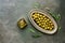 Green olives in olive oil, metal plate, dark rustic background, decorated with leaves. Top view, flat lay, copy space