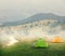 Green and orange tents on plain in mountains on foggy morning