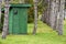 A green outhouse near a pine tree planted in a Lin
