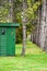 A green outhouse in a pine forest